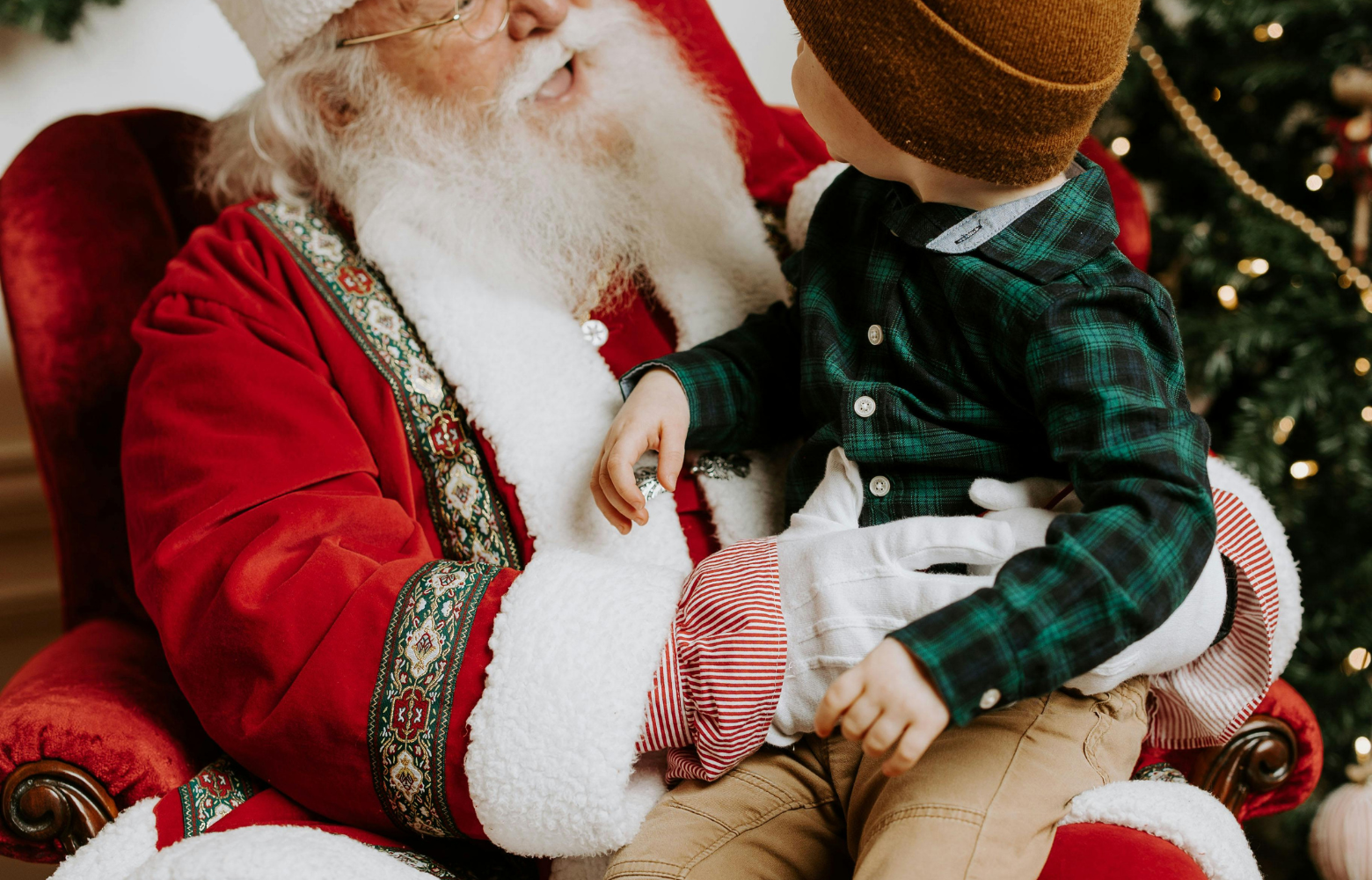 A young child sits on Santa's lap, smiling with excitement as they share a special holiday moment during the Cookies with Santa event.