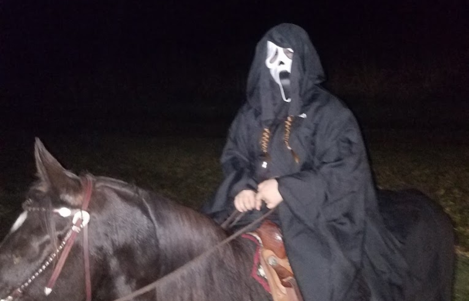 A person wearing a ghost mask rides a horse, blending eerie and mysterious elements into the Halloween-themed scene.