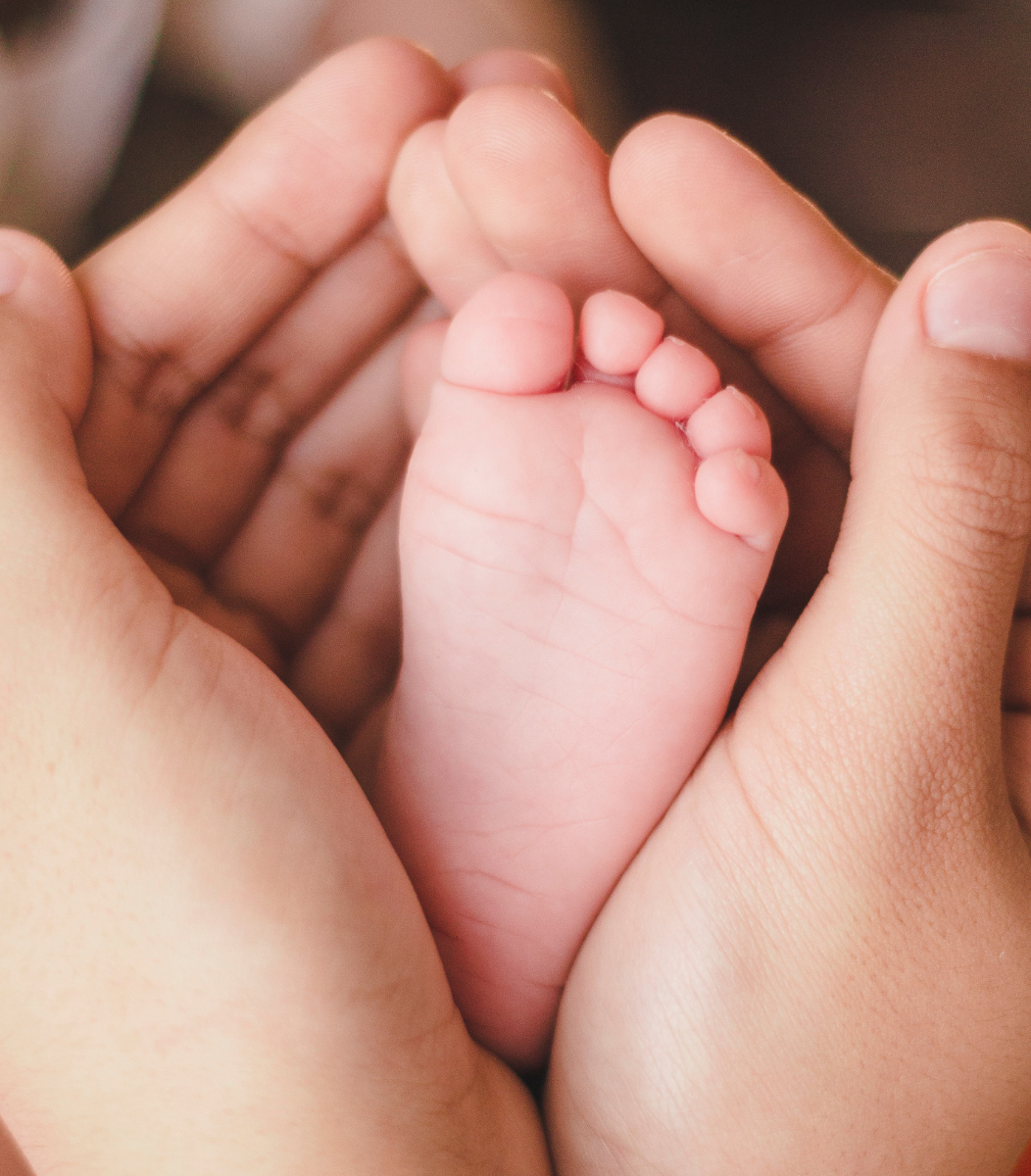 A parent's hand gently cradling a baby's tiny foot, symbolizing the love and care celebrated during baby showers hosted by Cavanaugh Carriages